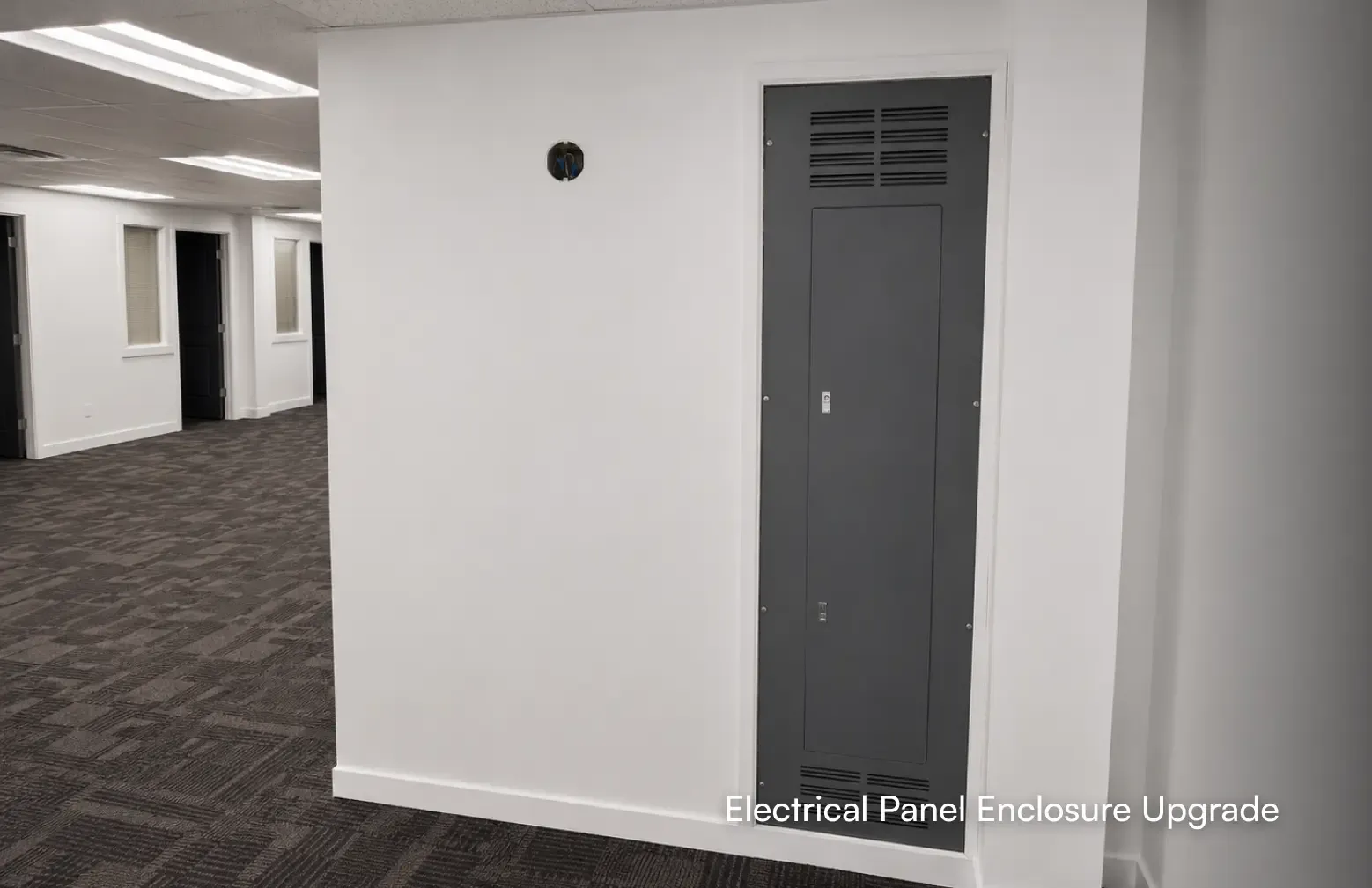 Close-up of a newly upgraded commercial electrical panel enclosure installed on a white wall in a freshly renovated open workspace by PCC Renovations.